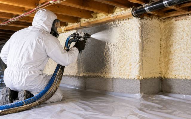 Installer spraying closed cell foam along a foundation wall over a taped ground sheet
