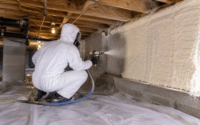 Installer sealing a crawl space wall in full protective kit