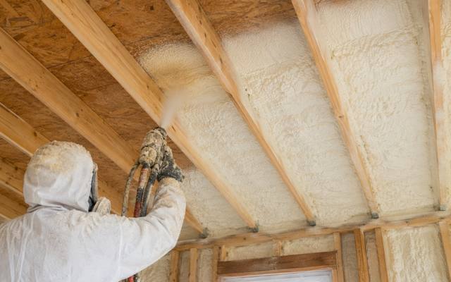 Foam going onto a roof deck between the rafters of an outbuilding